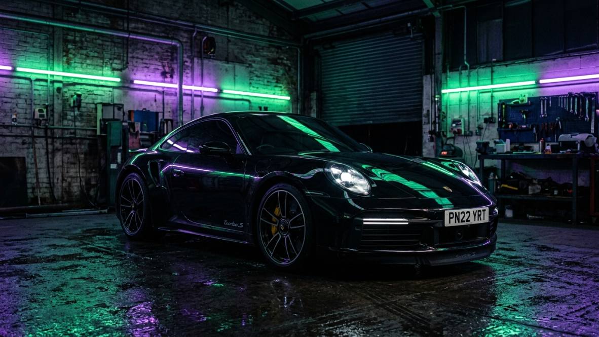 Black Porsche 911 with tinted windows in a neon garage
