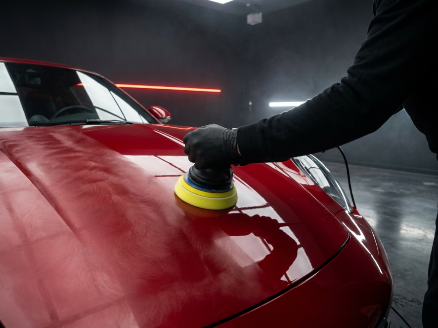Machine polisher on a red hood, half hazy with swirl marks and half mirror gloss